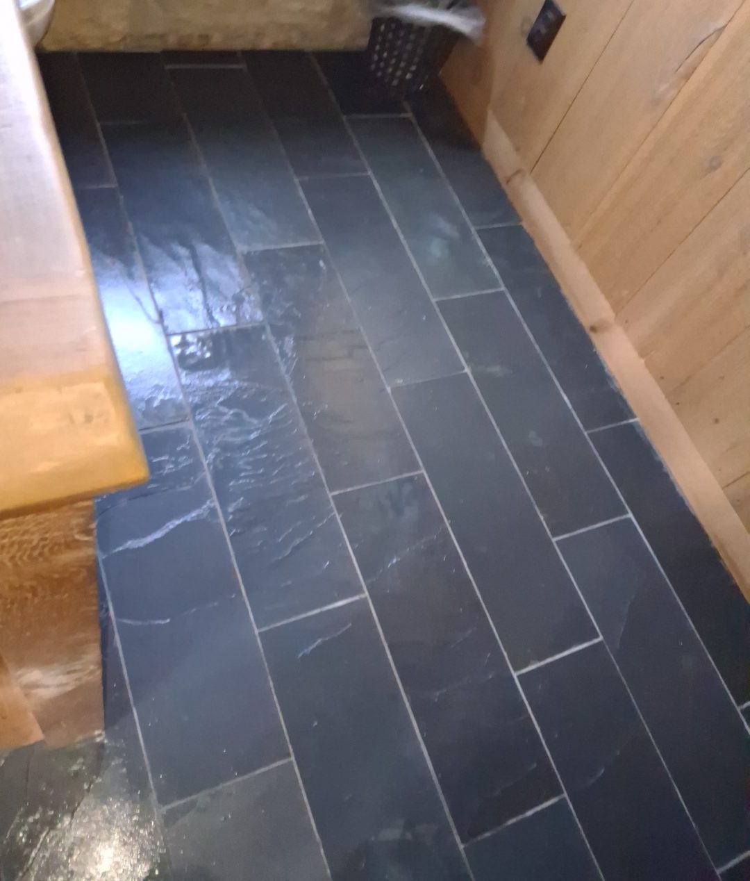 Slate tile floor cleaned to a sheen beside natural wood paneling