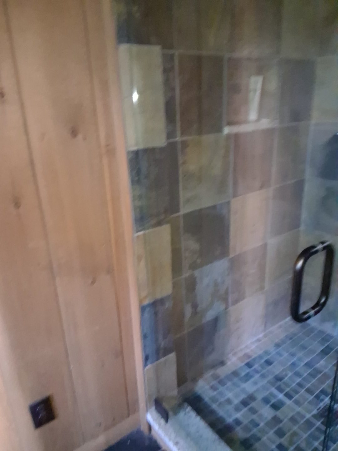 Stone tile shower wall and glass door edge after final detail cleaning